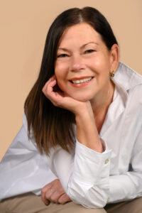 Regina Koch lächelnd, sitzt mit Kopf auf die Hand gestützt